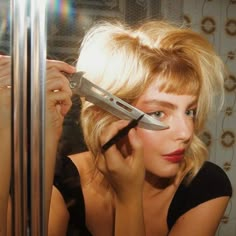 a woman holding a knife in front of her face and looking into the mirror while she is getting ready to cut her hair