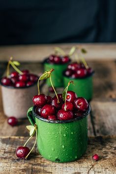 three small cups filled with cherries on top of a wooden table