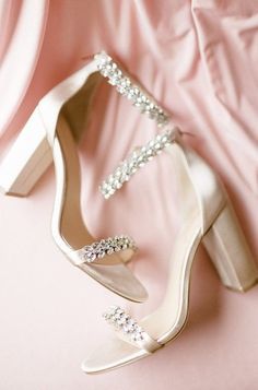 a pair of white high heeled shoes sitting on top of a pink satin surface