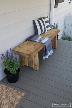 a wooden bench sitting on top of a porch next to a planter filled with flowers