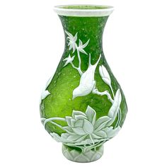 a green glass vase with white flowers and leaves on it's sides, sitting in front of a white background