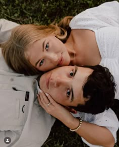 two people laying on the ground with their arms around each other and looking at the camera