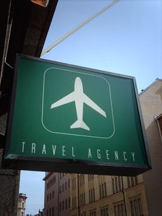 a green sign hanging from the side of a building that says travel agency on it