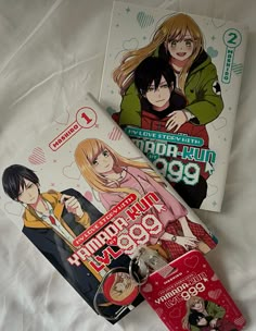 two anime books laying on top of a white bed next to each other with tags hanging from them