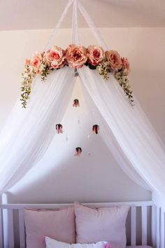 a canopy bed with pink flowers hanging from it's sides and pillows on the bottom