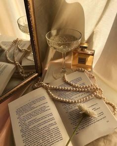 an open book with pearls and a flower on it next to a glass bowl filled with water