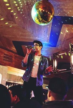 a man standing in front of a disco ball on top of a dance floor while holding a microphone