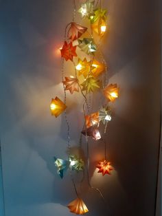 an origami star hanging on a wall with some lights attached to the chain