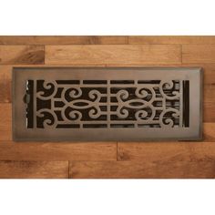 the floor register is made from metal and has scroll designs on it, along with wood floors