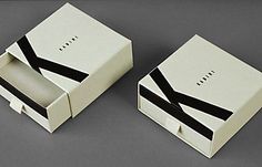 two white boxes with black ribbons on them, one opened and the other closed up