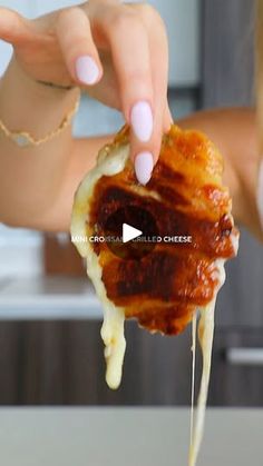 a woman is holding up a pastry with cheese and sauce on it to the camera