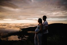 a pregnant couple standing on top of a mountain