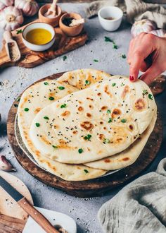 two flat breads on a wooden board with garlic and oil in the back ground