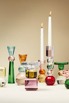 many different colored glass objects and candles on a white table with one candle in the middle