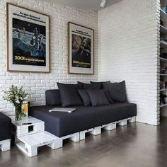 a living room with white brick walls and black couches, two framed movie posters on the wall