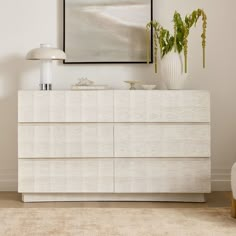 a white dresser sitting in a living room next to a lamp and painting on the wall