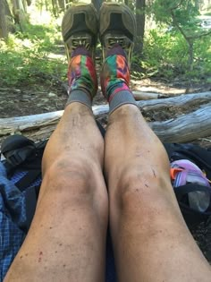 the legs and feet of a man who is sitting on a blanket in the woods