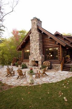 a log cabin with stone patio and seating area in the front yard is surrounded by greenery