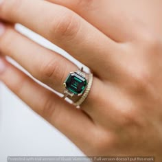 a woman's hand wearing a ring with an emerald and diamond center stone on it