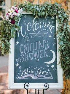 a baby shower sign with greenery on it