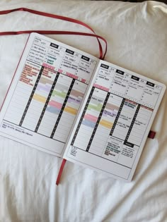 an open planner book sitting on top of a bed next to a red ribbon and pillow