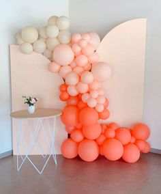 an arrangement of balloons is displayed in front of a white wall and table with a vase on it