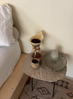 a small table with two cups on it next to a white bed and a pillow