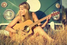 a woman sitting in the grass with an acoustic guitar next to a vw bus