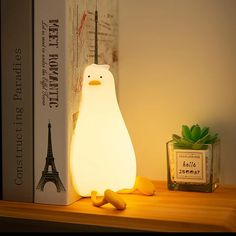 a white penguin lamp sitting on top of a wooden shelf next to a bookcase