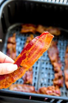 bacon strips being held up to the side of an open bbq with meat on it