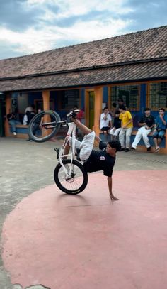 a man doing a handstand on a bicycle in front of a building with people watching