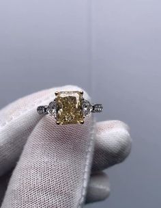 a fancy yellow diamond ring with three diamonds on it's sides, sitting in a gloved hand