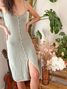 a woman standing in front of a plant wearing a dress with buttons on the side