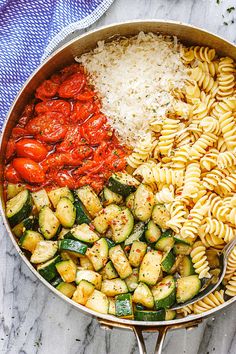 a pan filled with different types of pasta and vegetables on top of a marble counter