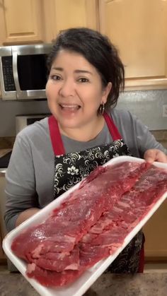 a woman holding up a tray of raw meat