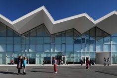 people are walking around in front of a building with glass walls and triangular shaped windows