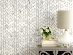 a nightstand with a lamp and flowers on it in front of a wallpapered background