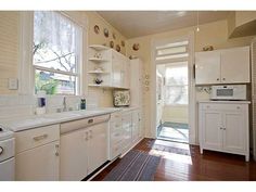 a kitchen with white cabinets and wood flooring next to an open door that leads to a patio