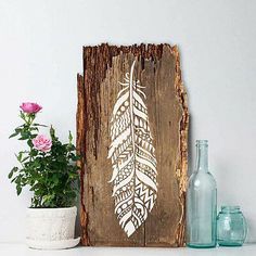 a wooden sign with a white feather on it next to some vases and flowers