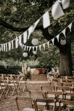 an outdoor wedding setup with wooden chairs and paper lanterns hanging from the trees in front of it