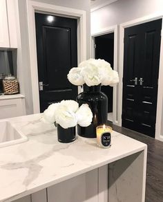 a white marble counter top with flowers in black vases and candles on the counter