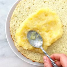 a person holding a spoon over a piece of bread on a white plate with butter