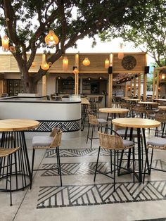 an outdoor dining area with tables, chairs and lights hanging from the trees in front of it