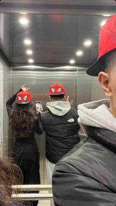 a group of people standing in front of a mirror wearing red hats and black jackets