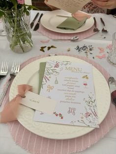 the table is set with pink and white plates, silverware, and menu cards