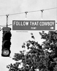 black and white photograph of a street sign that says follow that cowboy pkwy