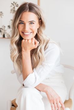 a woman sitting in a chair with her hand on her chin and smiling at the camera