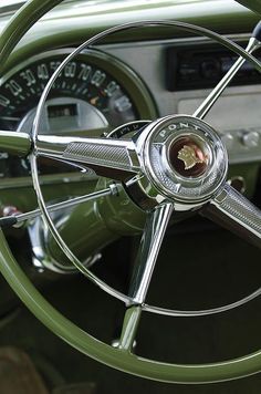 the steering wheel and dashboard of an old green car with chrome spokes on it