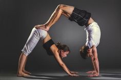 two people doing yoga poses in front of a dark background