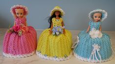 three crocheted dolls are sitting next to each other on a table with flowers